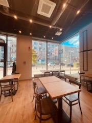 Jasne, przestronne wnętrze biurowe po malowaniu, widoczne drewniane podłogi, stoliki i krzesła, duże okna z widokiem na miasto, białe ściany z szarymi akcentami, sufit z oświetleniem punktowym...