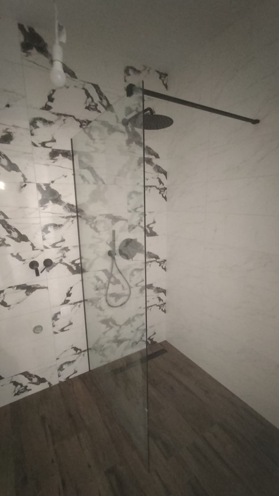 Nowoczesna kabina prysznicowa z czarną armaturą, szklaną ścianką i marmurowymi płytkami na ścianach oraz drewnopodobną podłogą.