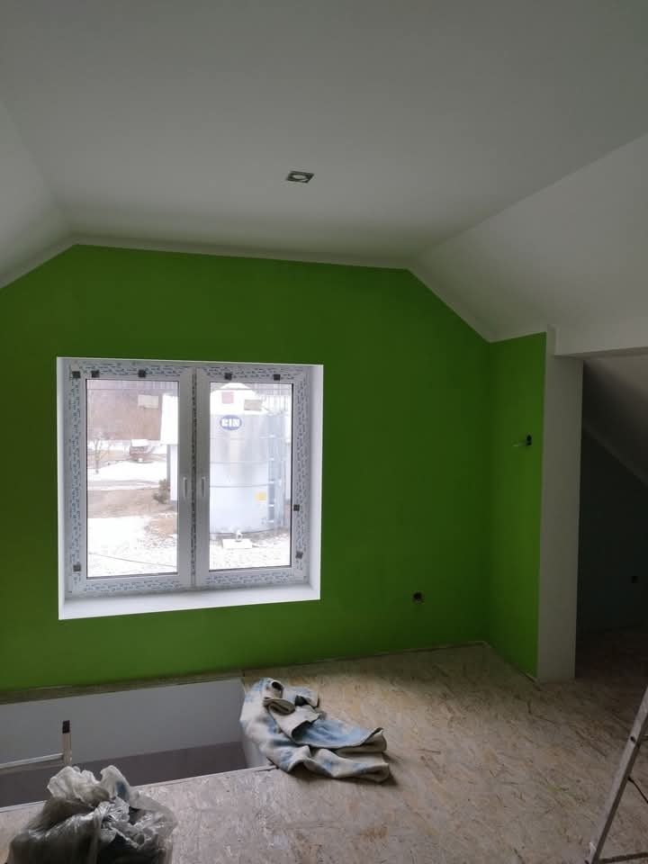 Świeżo pomalowane na zielono poddasze z białym oknem PCV i fragmentem podłogi z płyty OSB, widoczne ślady po pracy.
