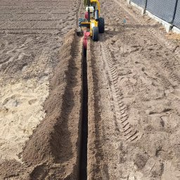 Klaron Michał Klawe - Wykopywanie rowu pod system nawadniania w Dąbrowie za pomocą glebogryzarki. Widoczny pracownik obsługujący maszynę i świeżo wykopany rów w ziemi.