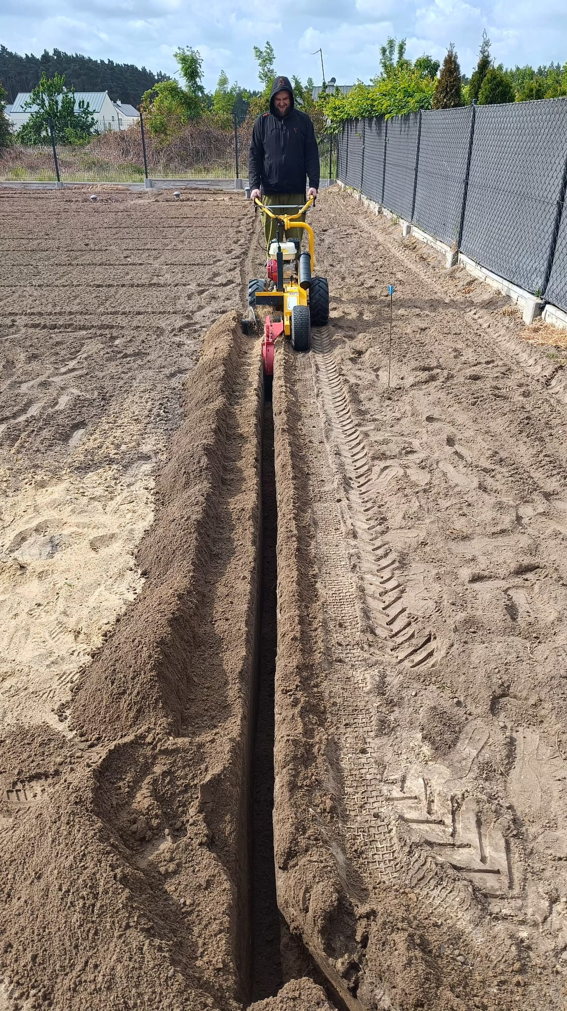 Wykopywanie rowu pod system nawadniania w Dąbrowie za pomocą glebogryzarki. Widoczny pracownik obsługujący maszynę i świeżo wykopany rów w ziemi.