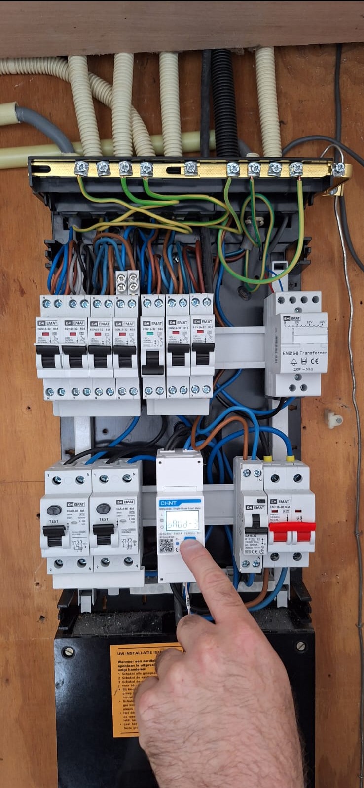 Rozdzielnica elektryczna z zamontowanymi bezpiecznikami i licznikiem energii, osoba palcem wskazuje na wyświetlacz licznika.
