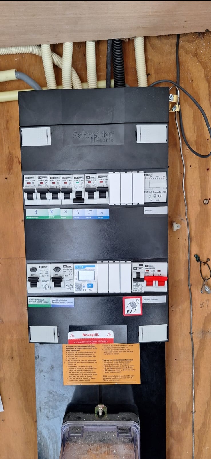 Rozdzielnica elektryczna Schneider Electric z zabezpieczeniami i naklejkami informacyjnymi, zamontowana na drewnianej ścianie w Miłobądzu, z widocznymi przewodami w peszlach.