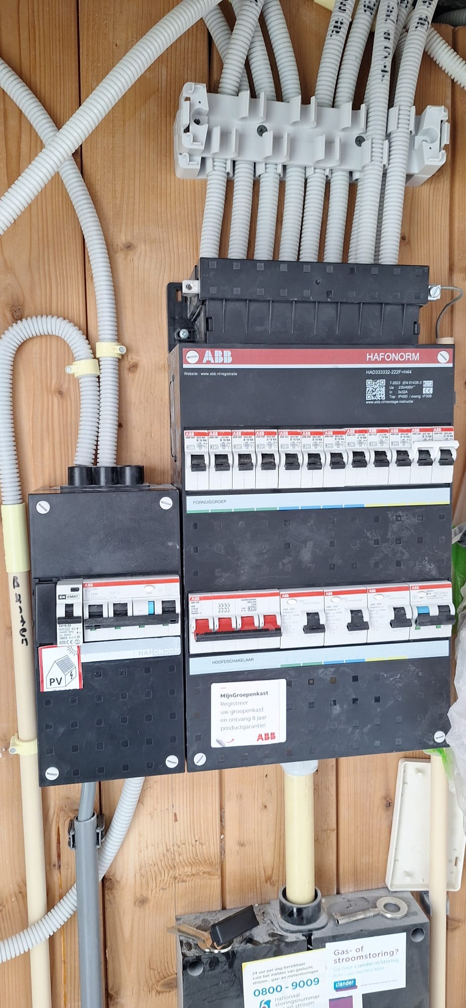 Szczegółowe ujęcie rozdzielnicy elektrycznej ABB z zainstalowanymi bezpiecznikami i przewodami w peszlach, zamontowanej na drewnianej ścianie.