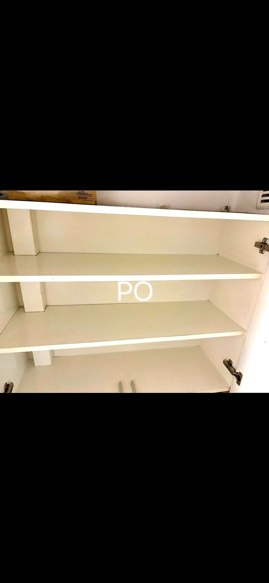 Wnętrze białej szafki z trzema pustymi półkami po czyszczeniu, widoczne zawiasy i ślady po naklejce na środkowej półce.