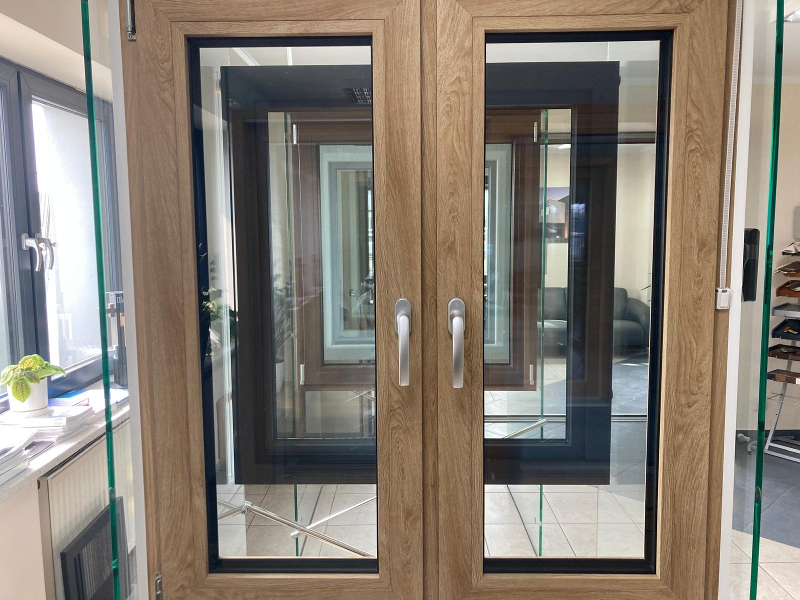 Dwuskrzydłowe okno z drewnopodobną ramą, widoczne uchwyty i ekspozycja innych modeli w tle.