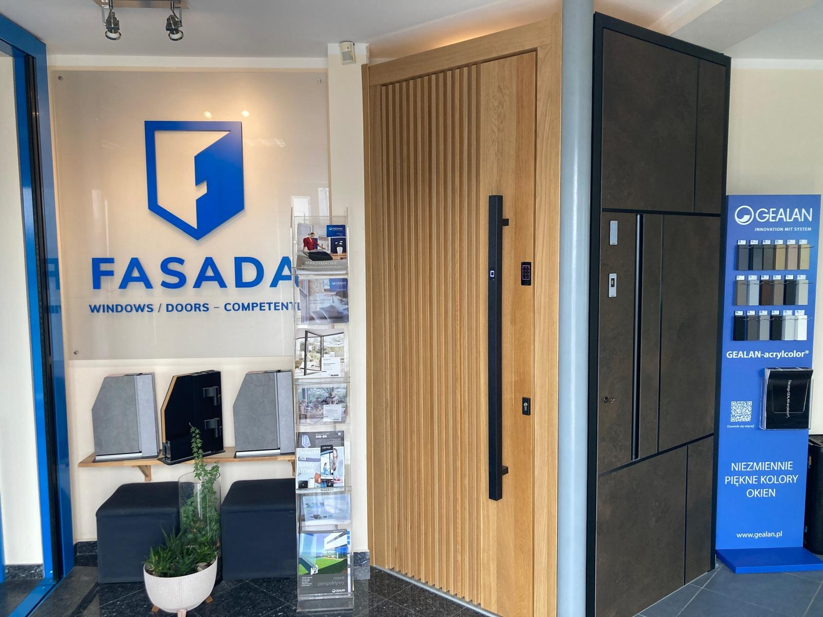 Ekspozycja dwóch modeli drzwi w salonie: jasne drzwi z pionowymi frezami i długim czarnym uchwytem oraz ciemne drzwi z panelem kolorów Gealan.