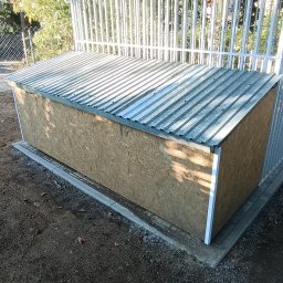 SpawajTo Grzegorz Marcinów - Zewnętrzna drewniana skrzynia z blachą falistą na dachu, umieszczona na betonowej podstawie przy metalowym ogrodzeniu panelowym.