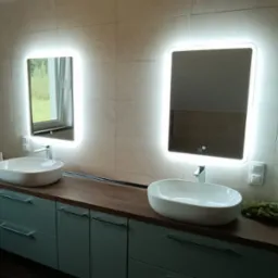 Nowoczesna łazienka z dwoma owalnymi umywalkami nablatowymi, podświetlanymi lustrami, szafkami w odcieniach błękitu i pralką.