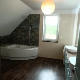 Nowoczesna łazienka na poddaszu z narożną wanną, deszczownicą, umywalkami nablatowymi i podświetlaną kulistą lampą.