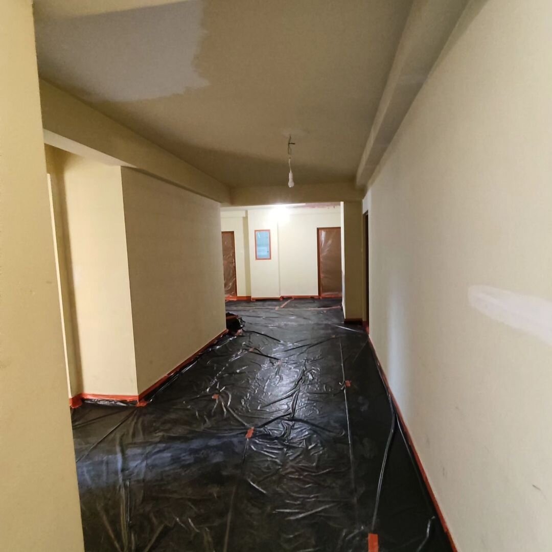 Klatka schodowa w bloku zabezpieczona folią malarską przed odświeżeniem ścian, widoczne fragmenty świeżo pomalowanego sufitu.