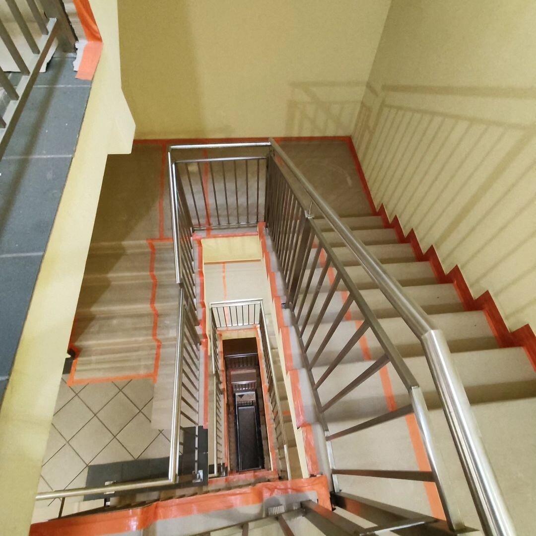 Klatka schodowa w bloku mieszkalnym zabezpieczona taśmą malarską przed malowaniem ścian i schodów, widok z góry.