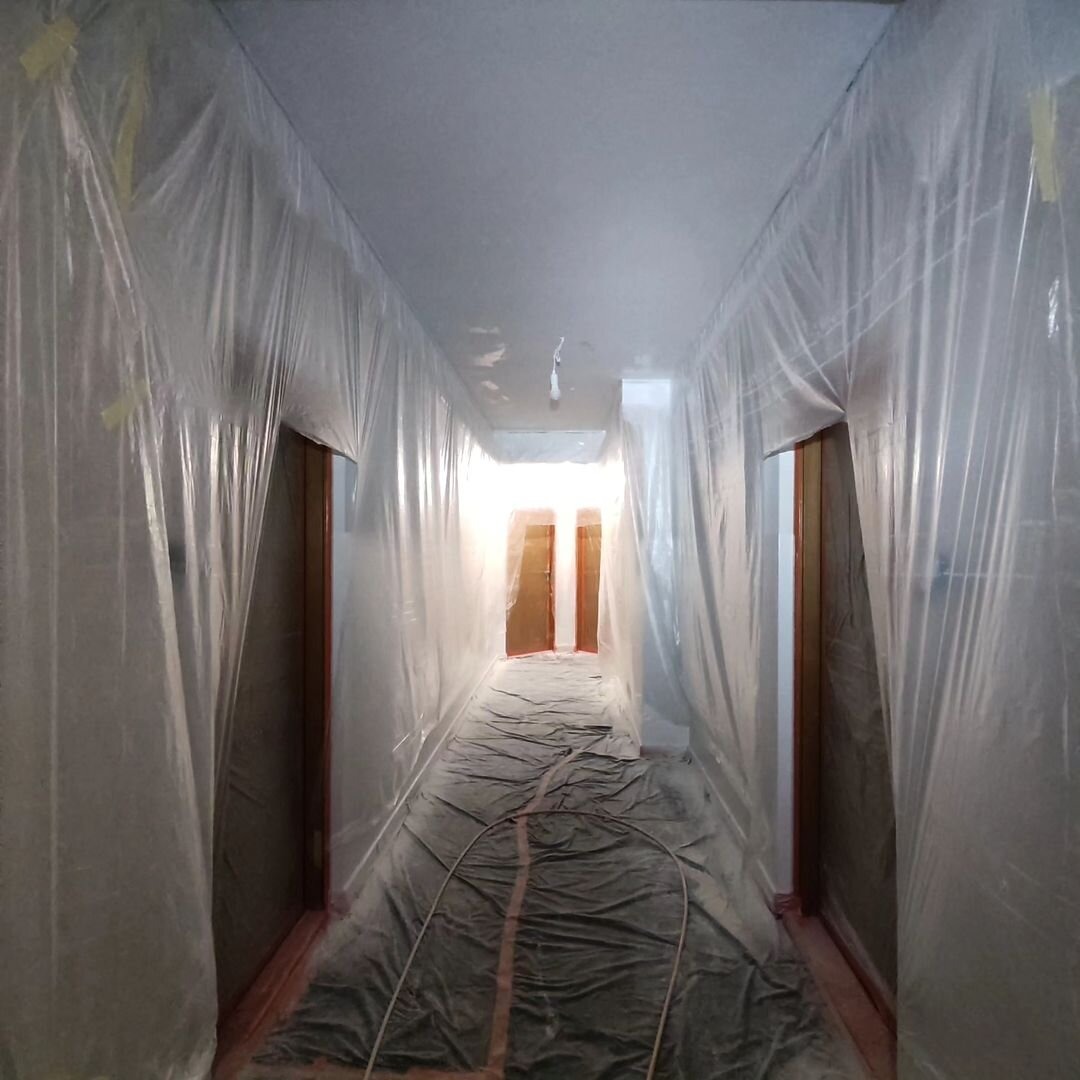 Korytarz w trakcie przygotowania do malowania w Warszawie, zabezpieczony folią ochronną na podłodze, ścianach i drzwiach.