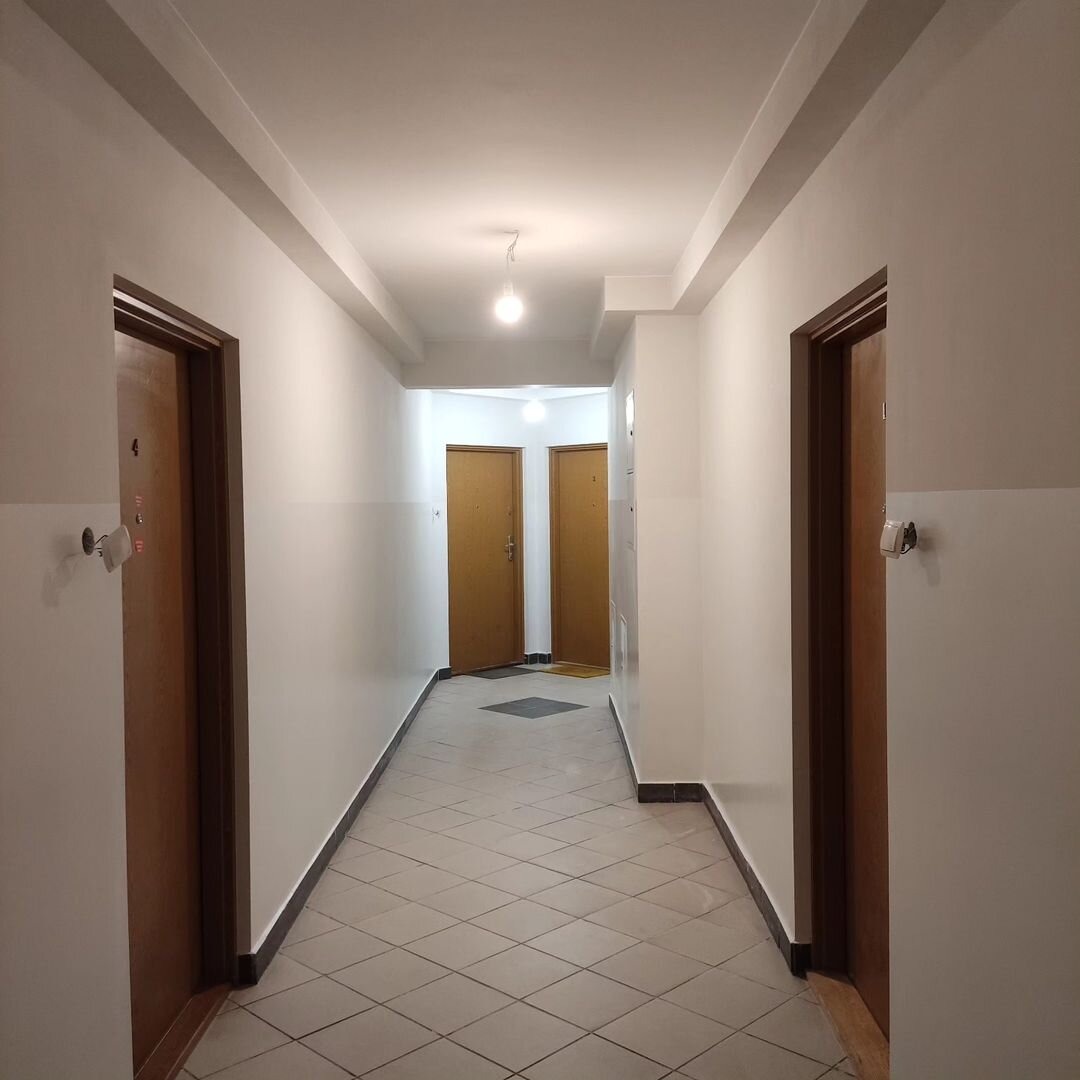 Wnętrze pomalowanej na biało klatki schodowej z brązowymi drzwiami i szarą podłogą z płytek