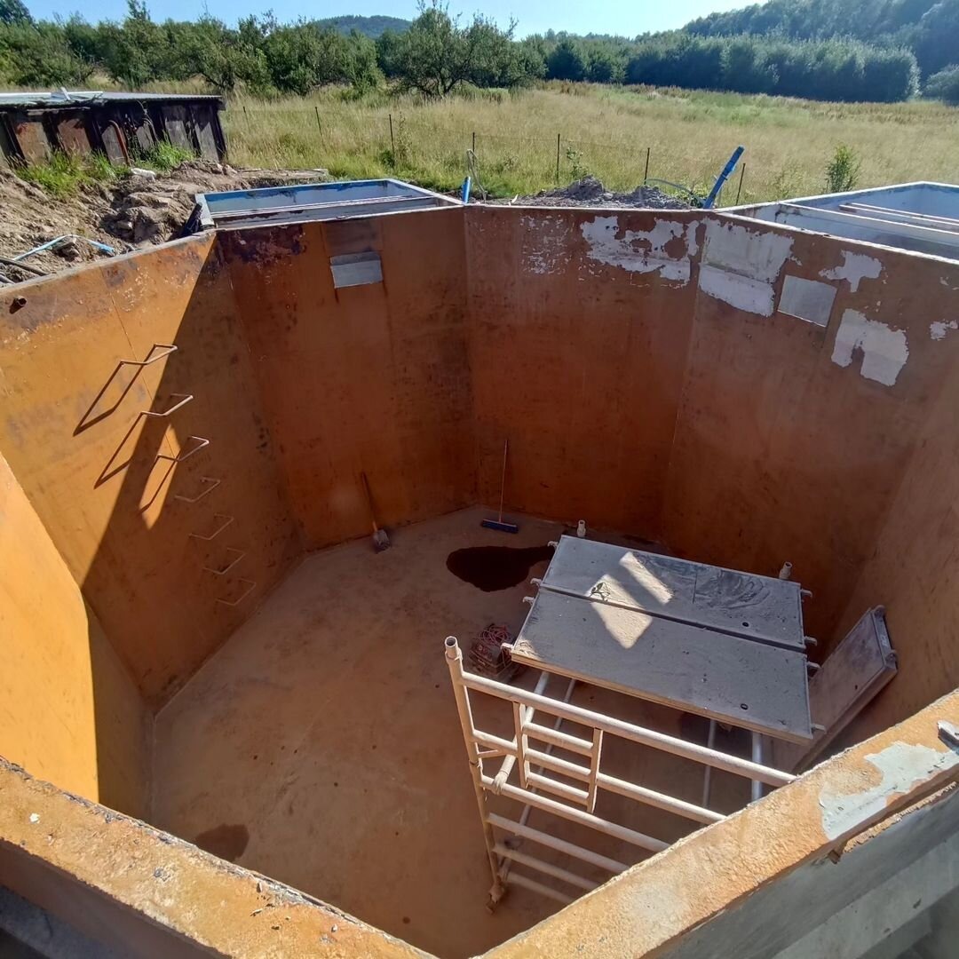 Wnętrze dużego, pomalowanego na pomarańczowo zbiornika z drabinką, śladami po łatach i rozlaną cieczą na dnie. Na dnie również stojące rusztowanie i leżące narzędzia.