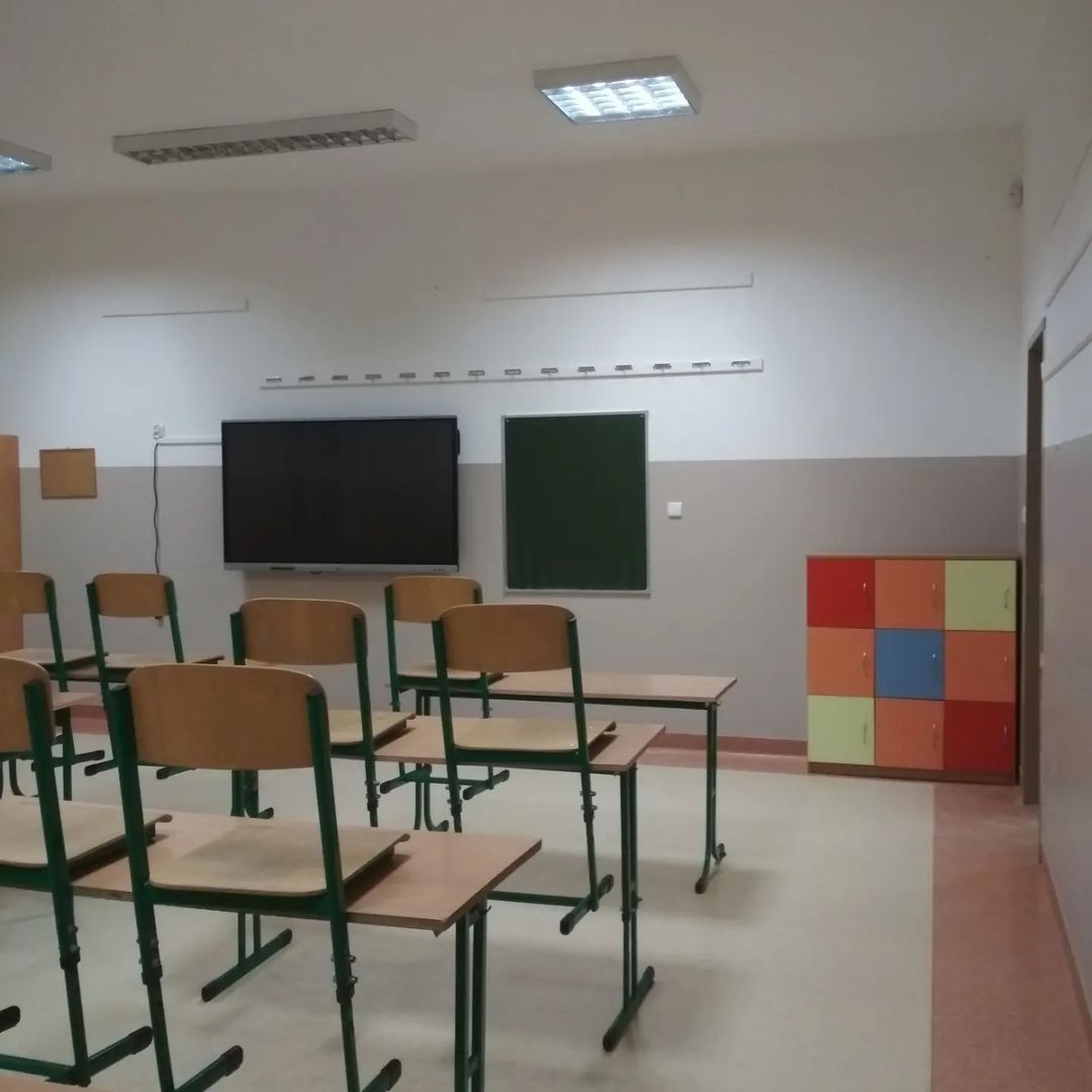 Wnętrze odnowionej klasy szkolnej z rzędami ławek, tablicą interaktywną i szafką w kolorowe kwadraty.