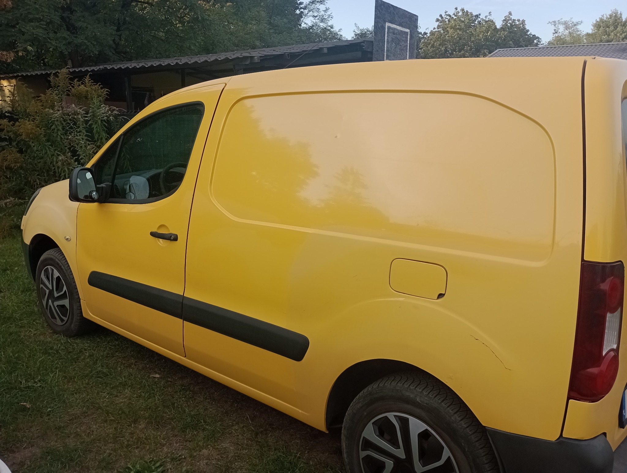 Żółty furgon dostawczy zaparkowany na trawie, widoczny z boku, zarysowania na tylnym panelu.