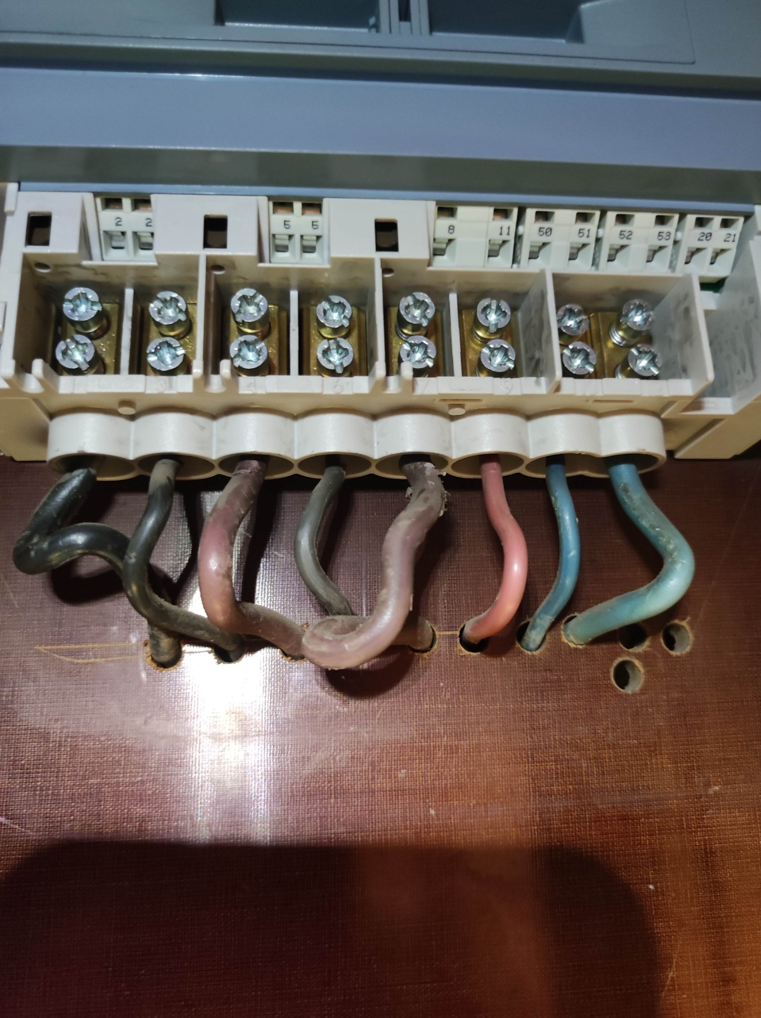 Przyłącze kabli o różnych kolorach do listwy zaciskowej w skrzynce elektrycznej, widoczne numery na listwie i ślady po wierceniu na drewnianej powierzchni.