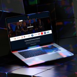 SKYLITE SPÓŁKA Z OGRANICZONĄ ODPOWIEDZIALNOŚCIĄ - Laptop wyświetla stronę internetową plebiscytu sportowego 2024 z logotypami sponsorów i zdjęciem laureatów, leżący na ciemnym, podświetlanym stole.