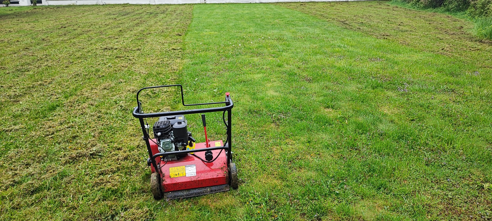 Aerator spalinowy na trawniku, widoczny fragment trawnika po aeracji, z resztkami darni na powierzchni
