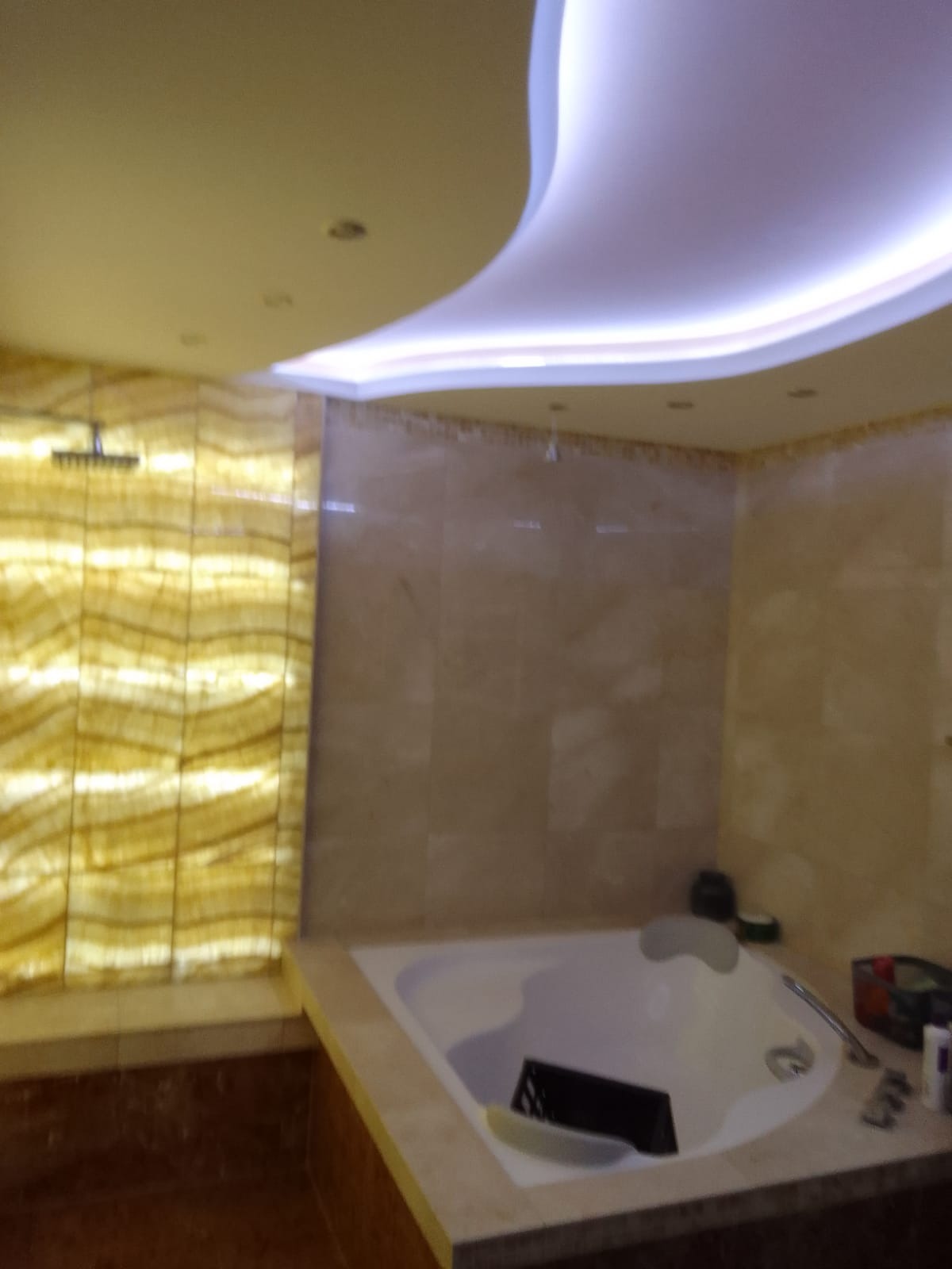 Luksusowa łazienka z podświetlaną ścianą z onyksu, wanna z hydromasażem i podwieszanym sufitem z oświetleniem LED.