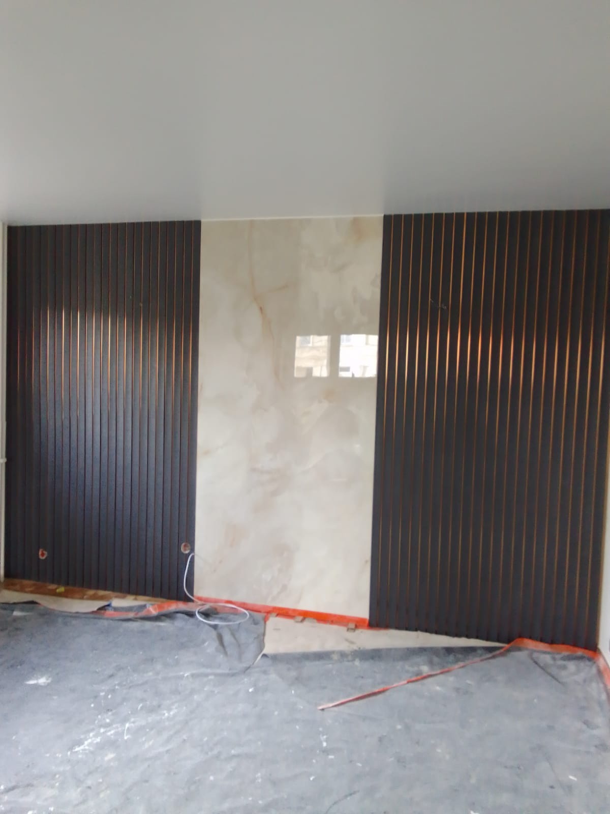 Montaż paneli ściennych z efektem lameli w kolorze ciemnego brązu, sąsiadujących z płytą imitującą marmur, zabezpieczona podłoga folią malarską.