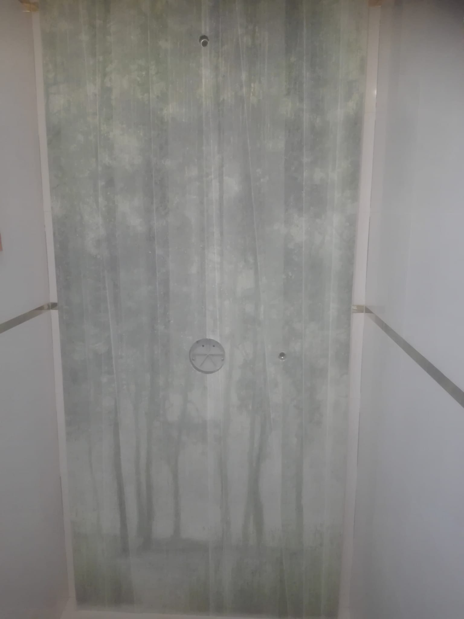 Wykończona łazienka z fototapetą przedstawiającą motyw leśny na ścianie prysznica, widoczne minimalistyczne srebrne listwy wykończeniowe.