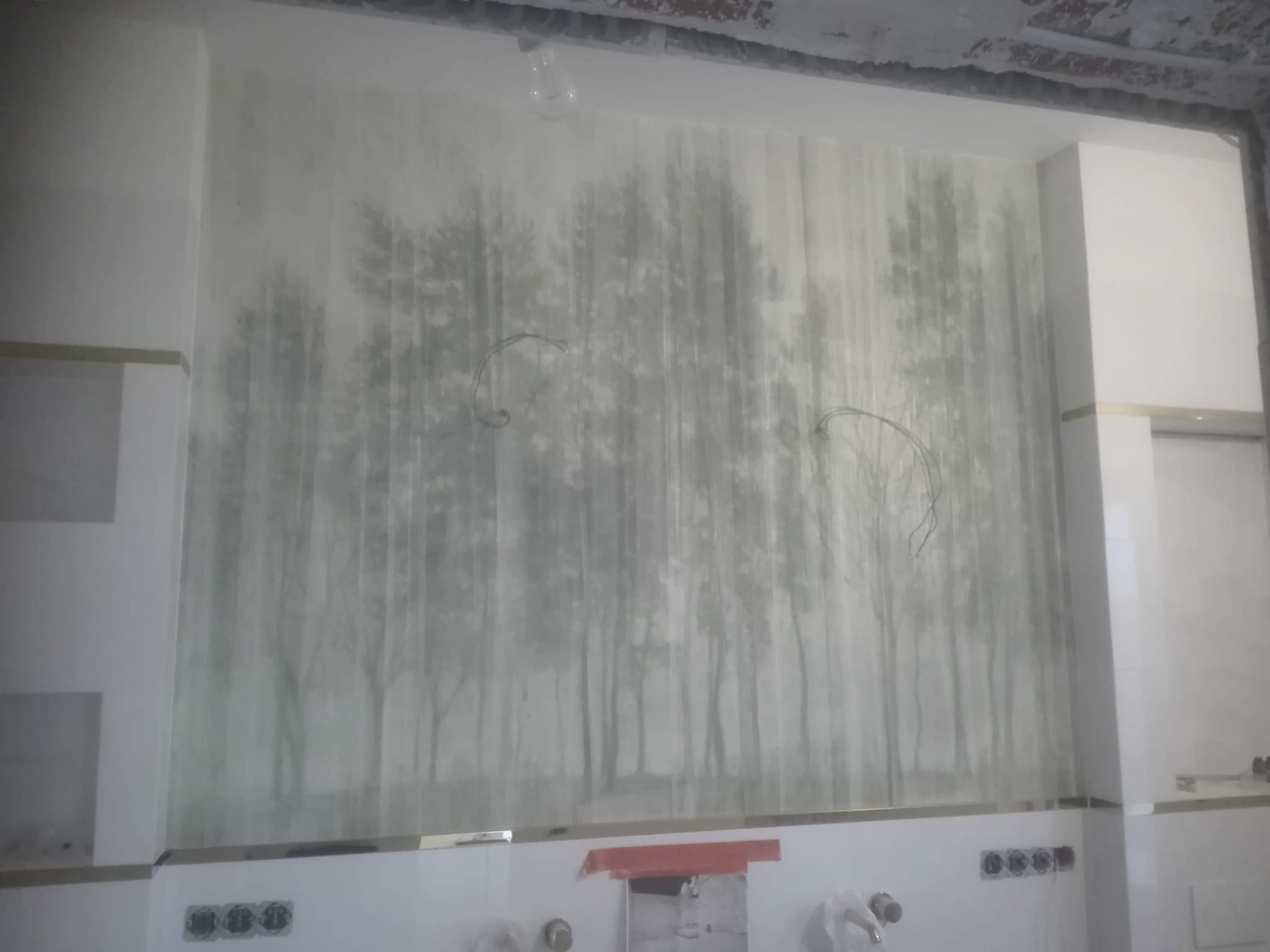 Ściana w trakcie wykańczania z dekoracyjnym malowaniem imitującym las we mgle, widoczne gniazdka elektryczne, surowy sufit i wystające przewody, fragment glazury.