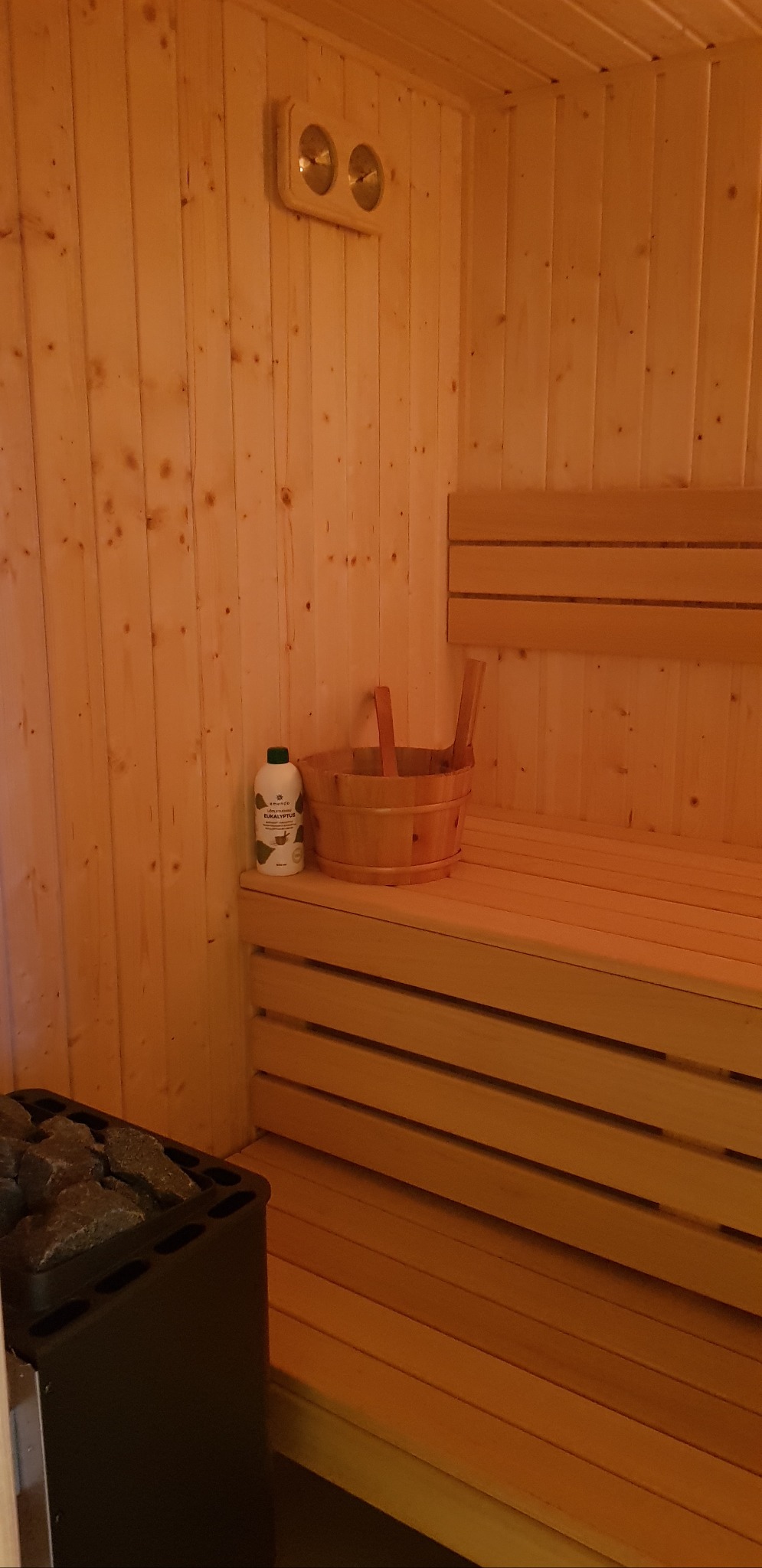 Wnętrze sauny z drewnianym wykończeniem, ławkami, piecem z kamieniami i akcesoriami do aromaterapii. Widok na detale wykończenia i wyposażenie sauny.