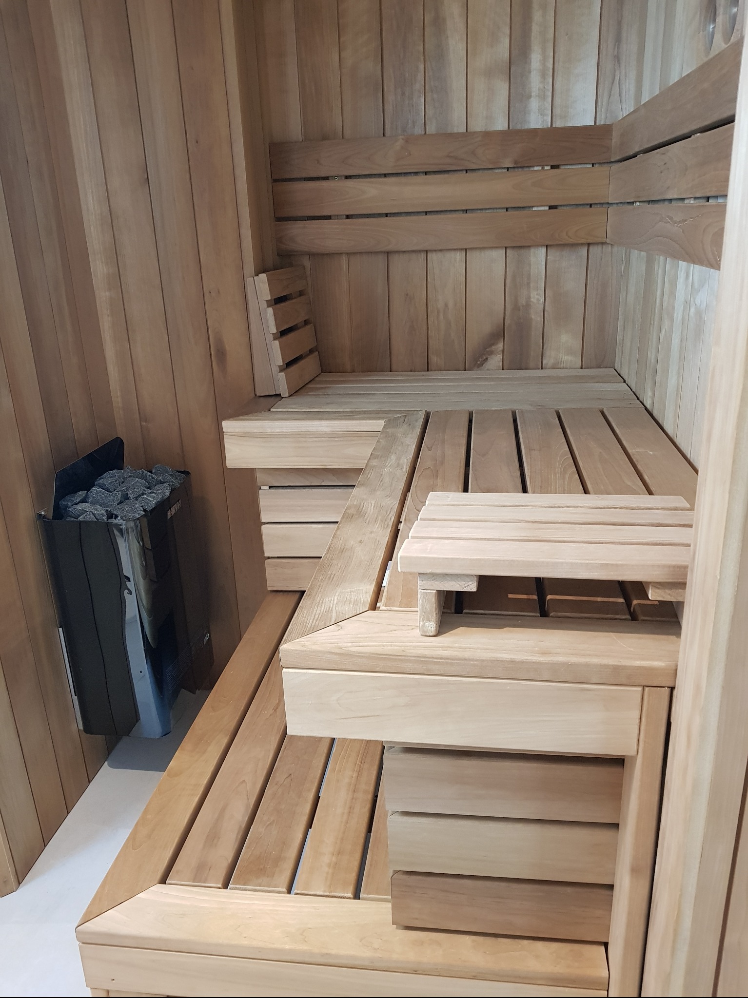 Wnętrze sauny wykończone drewnem, z piecem Harvia wypełnionym kamieniami. Widoczne drewniane ławki i oparcia, tworzące relaksującą atmosferę.