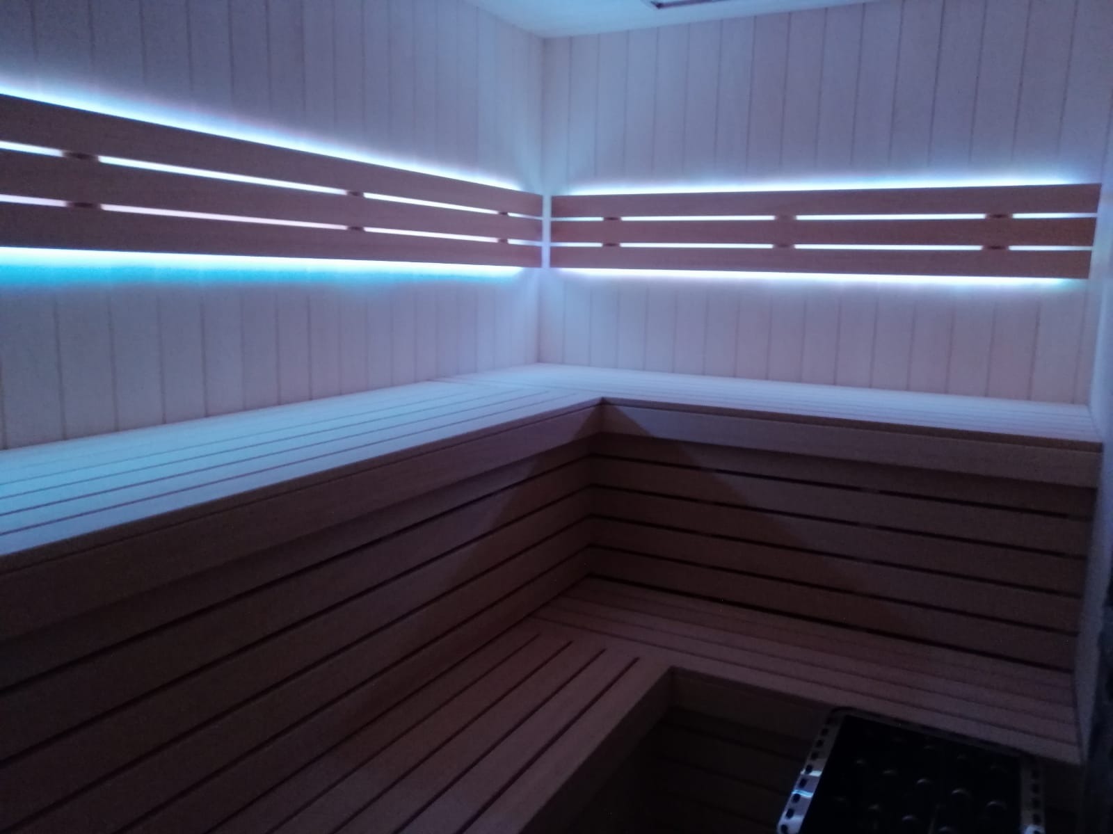 Wnętrze sauny z drewnianymi ławkami i panelami ściennymi, oświetlone niebieskim światłem LED, tworzące relaksującą atmosferę. Widok z perspektywy wnętrza.