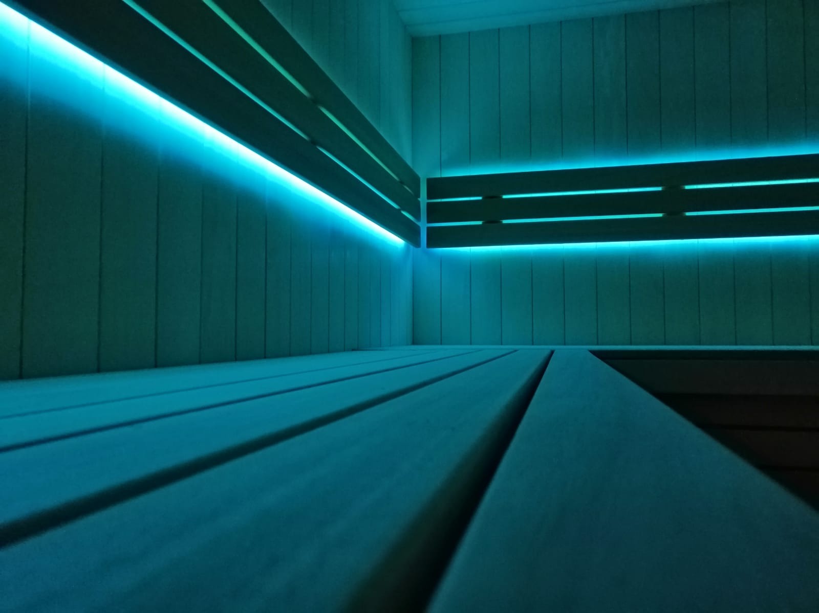 Nowoczesna sauna z drewnianymi ławkami i subtelnym, błękitnym oświetleniem LED podkreślającym minimalistyczny design wnętrza.