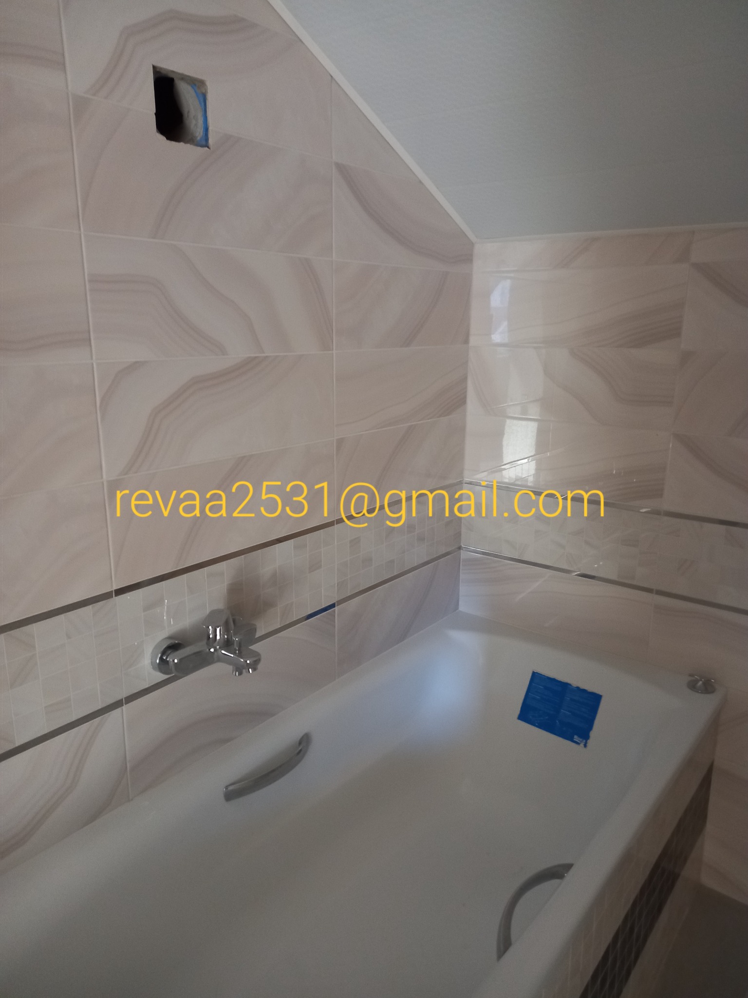 Wanna obudowana płytkami z dekoracyjnym pasem, widoczna bateria i otwór w ścianie z wystającymi przewodami.