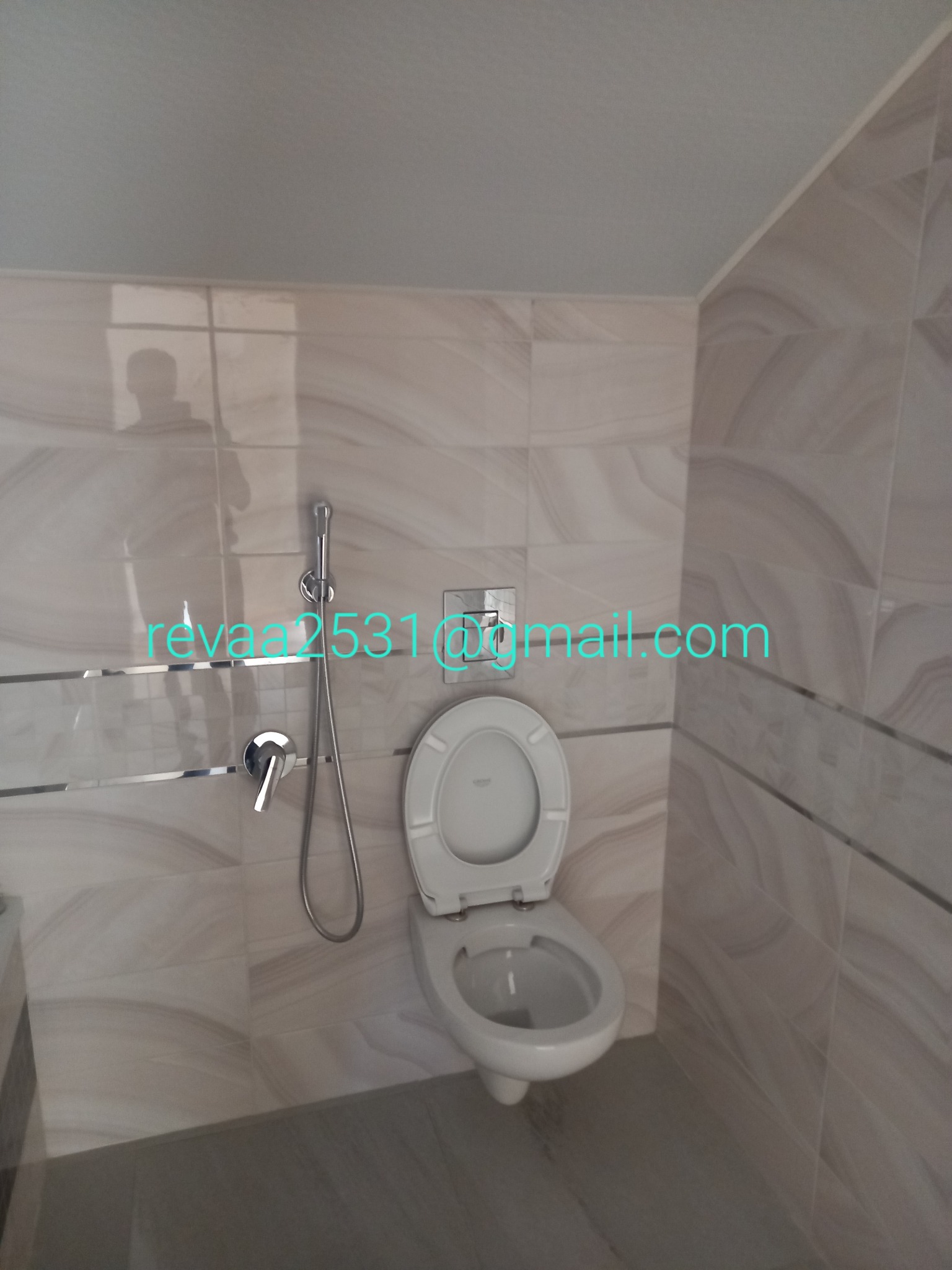 Wykończona łazienka z beżowymi płytkami imitującymi marmur, wisząca toaleta z otwartą klapą i chromowana bateria z bidetką.