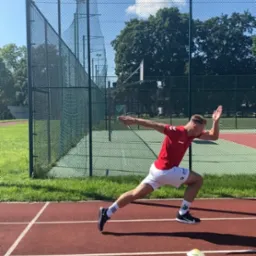 Biegacz w czerwonej koszulce i białych spodenkach w dynamicznej fazie startu na bieżni lekkoatletycznej, widoczny żółty pachołek.