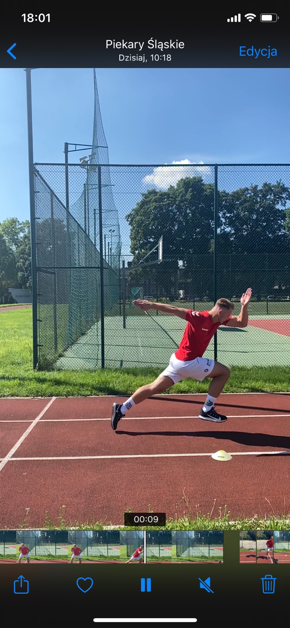 Biegacz w czerwonej koszulce i białych spodenkach w dynamicznej fazie startu na bieżni lekkoatletycznej, widoczny żółty pachołek.