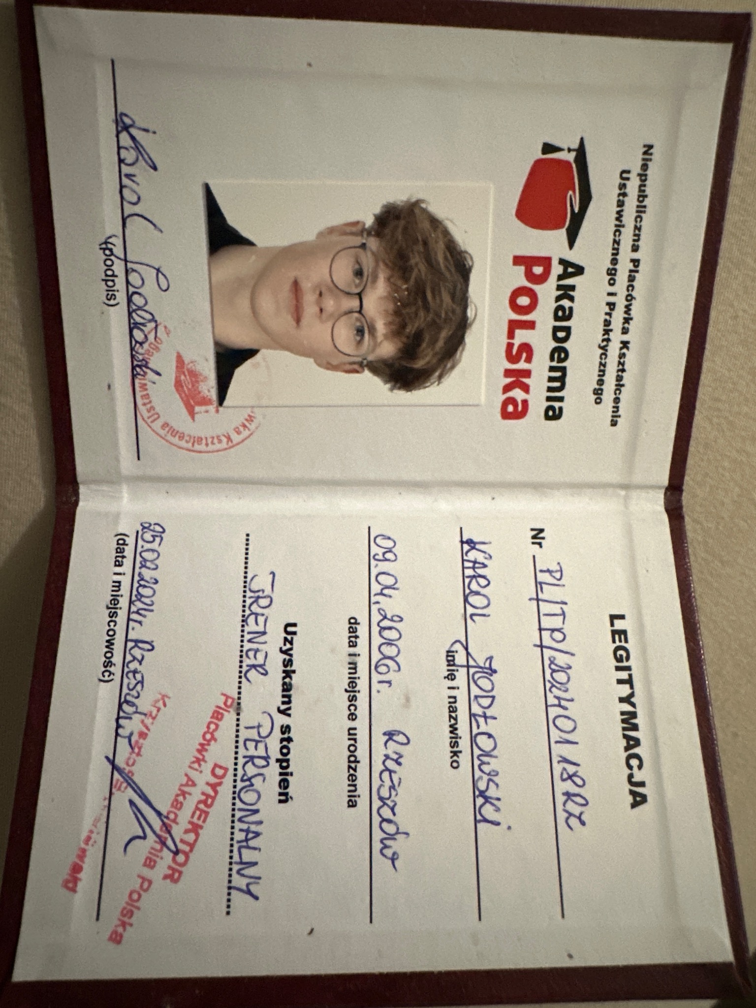 Otwarta legitymacja z fotografią młodego mężczyzny w okularach, poświadczająca uzyskanie stopnia Trenera Personalnego w Akademii Polska, z datą wydania i podpisem dyrektora.