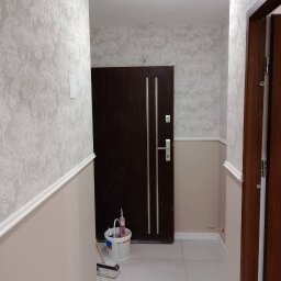 Ivan Pidhirnyi LW-STROJ - Korytarz po odświeżeniu ścian: dolna część pomalowana na beżowo, górna wytapetowana w delikatny wzór drzew, widoczne narzędzia malarskie przy drzwiach wejściowych.