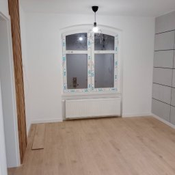 Ivan Pidhirnyi LW-STROJ - Wykończone wnętrze pokoju w Chorzowie po remoncie, z drewnianą podłogą, grzejnikiem pod łukowatym oknem i nowoczesną lampą wiszącą.