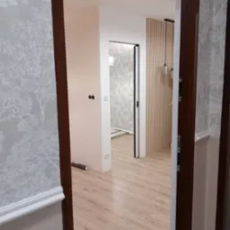 Widok na wykończone wnętrze mieszkania z nowymi panelami podłogowymi, tapetą w motywy drzew i ozdobną ścianą z drewnianych listew.
