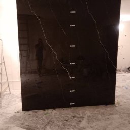 Ivan Pidhirnyi LW-STROJ - Czarna płyta z marmurkowym wzorem, zamocowana do ściany za pomocą tymczasowych kołków dystansowych, widoczna drabina i odbicie osoby robiącej zdjęcie.