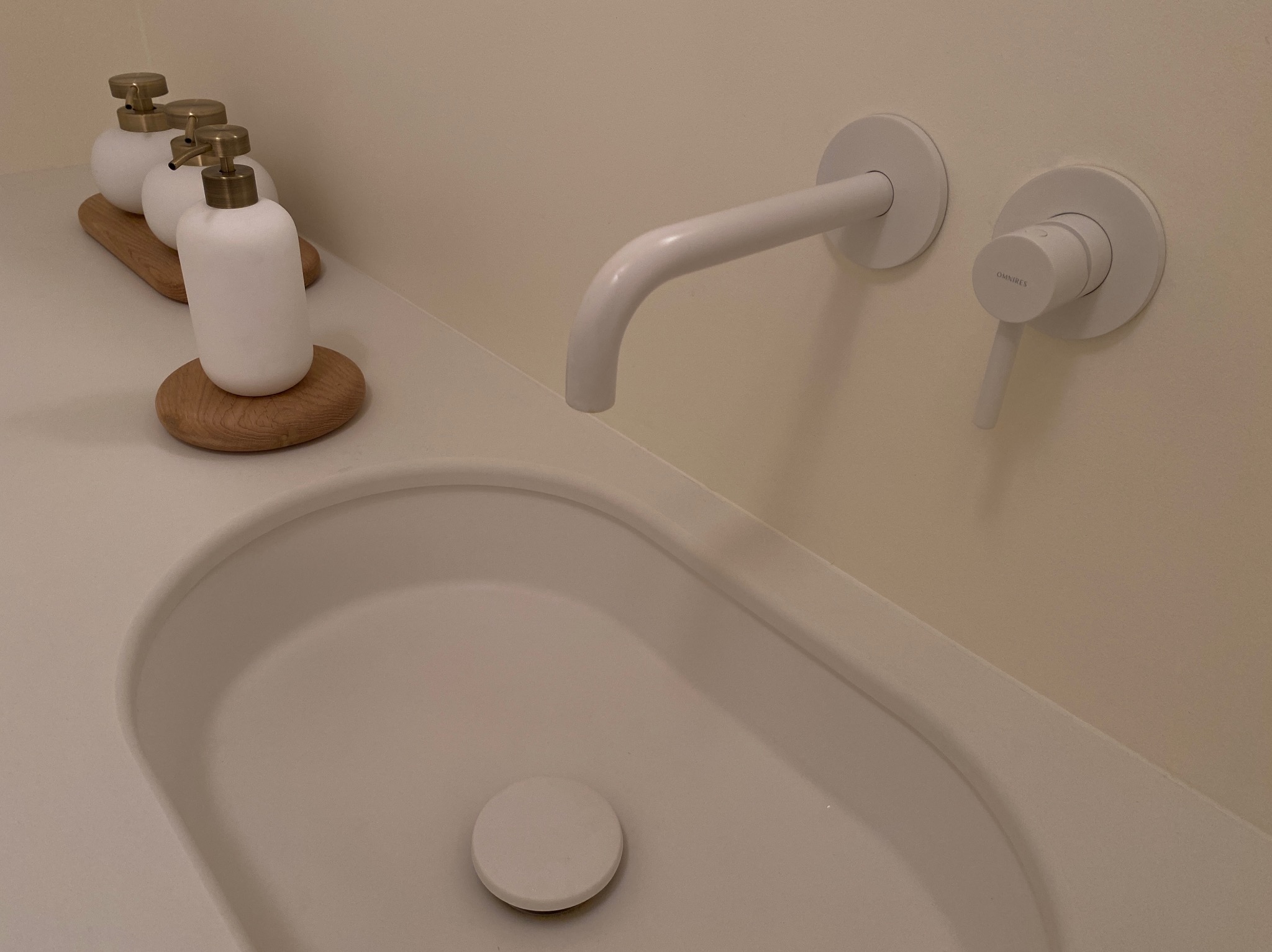 Minimalistyczna łazienka: biała umywalka z armaturą Omnires i dozowniki na drewnianej podstawie. Stonowana kolorystyka, nowoczesny design.