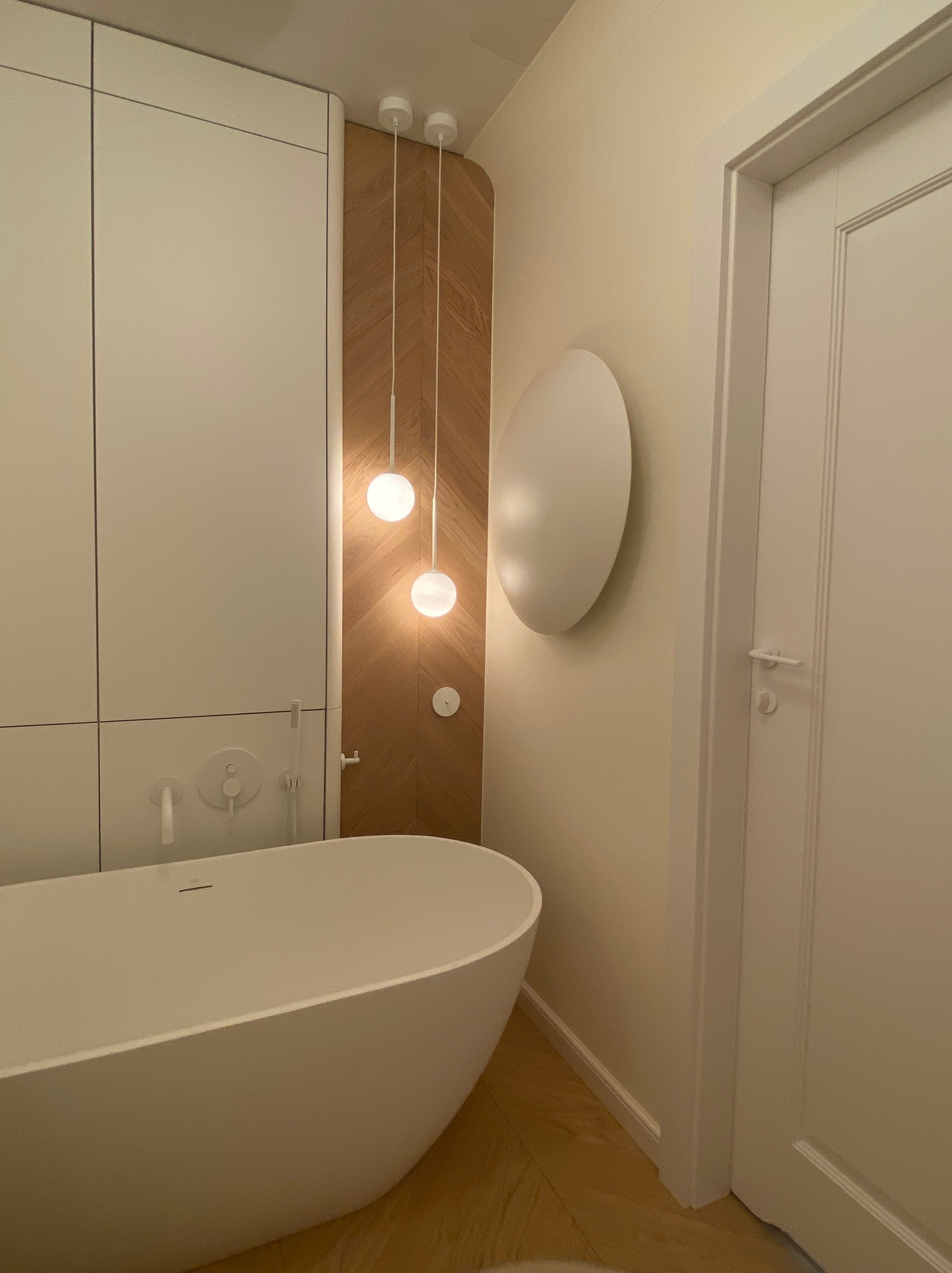 Nowoczesna łazienka z wolnostojącą białą wanną, drewnianymi akcentami i okrągłymi lampami wiszącymi. Minimalistyczny design i jasna kolorystyka.