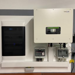 ELFOT GRZEGORZ PALIŃSKI - Zestawienie urządzeń: rozdzielnica elektryczna, falownik SOFAR Solar z wyświetlaczem i router TP-Link na ścianie z szarą listwą dekoracyjną.