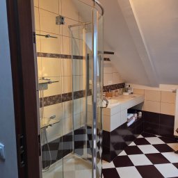 Czysta Magia - Ukończona łazienka na poddaszu z kabiną prysznicową, umywalką i czarno-białą podłogą w szachownicę. Widoczne płytki i akcesoria łazienkowe.