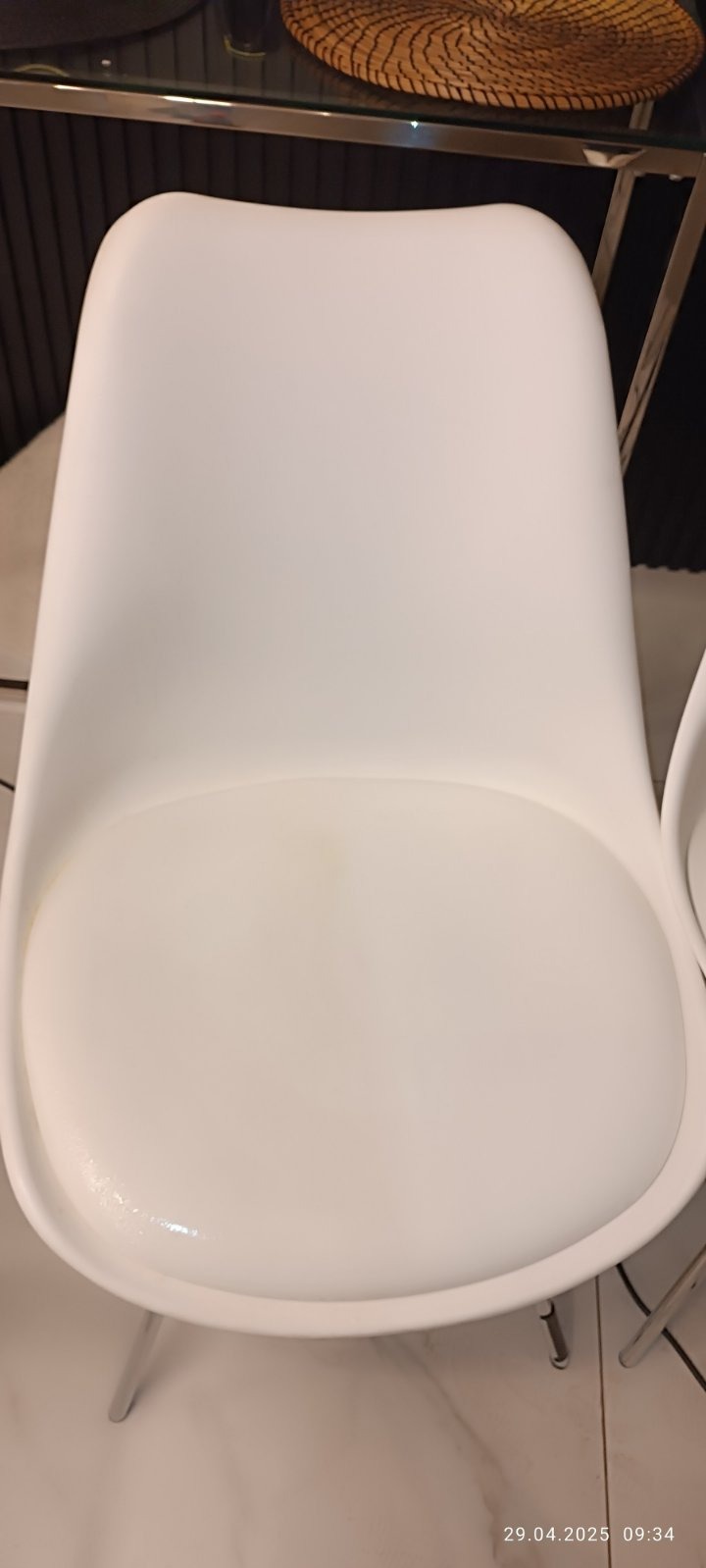 Białe krzesło z plamą na siedzisku, ustawione w pomieszczeniu z elementami dekoracyjnymi. Widok z góry, oświetlenie naturalne.