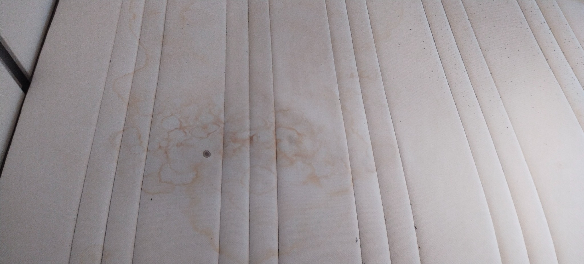 Beżowy materac z widocznymi, brązowymi plamami i zabrudzeniami, gotowy do prania. Widok z góry.