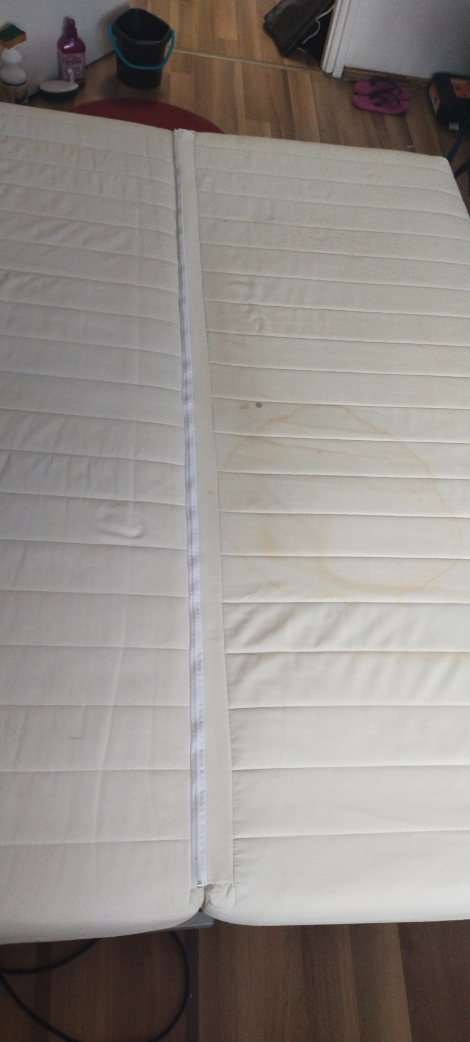 Materac z widocznymi plamami po jednej stronie i czystą po drugiej, oddzielone zamkiem błyskawicznym. Widoczny efekt czyszczenia.