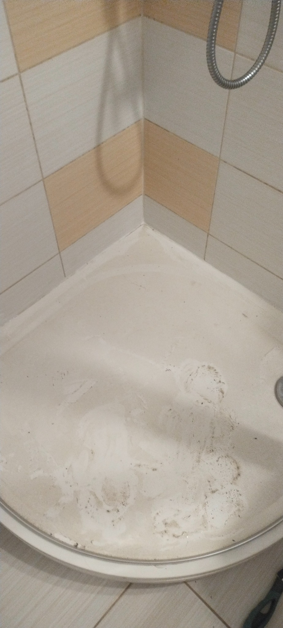 Brudny brodzik kabiny prysznicowej z widocznymi śladami po mydle i zaciekami, otoczony kafelkami w odcieniach beżu i brązu. Widoczna słuchawka prysznicowa.