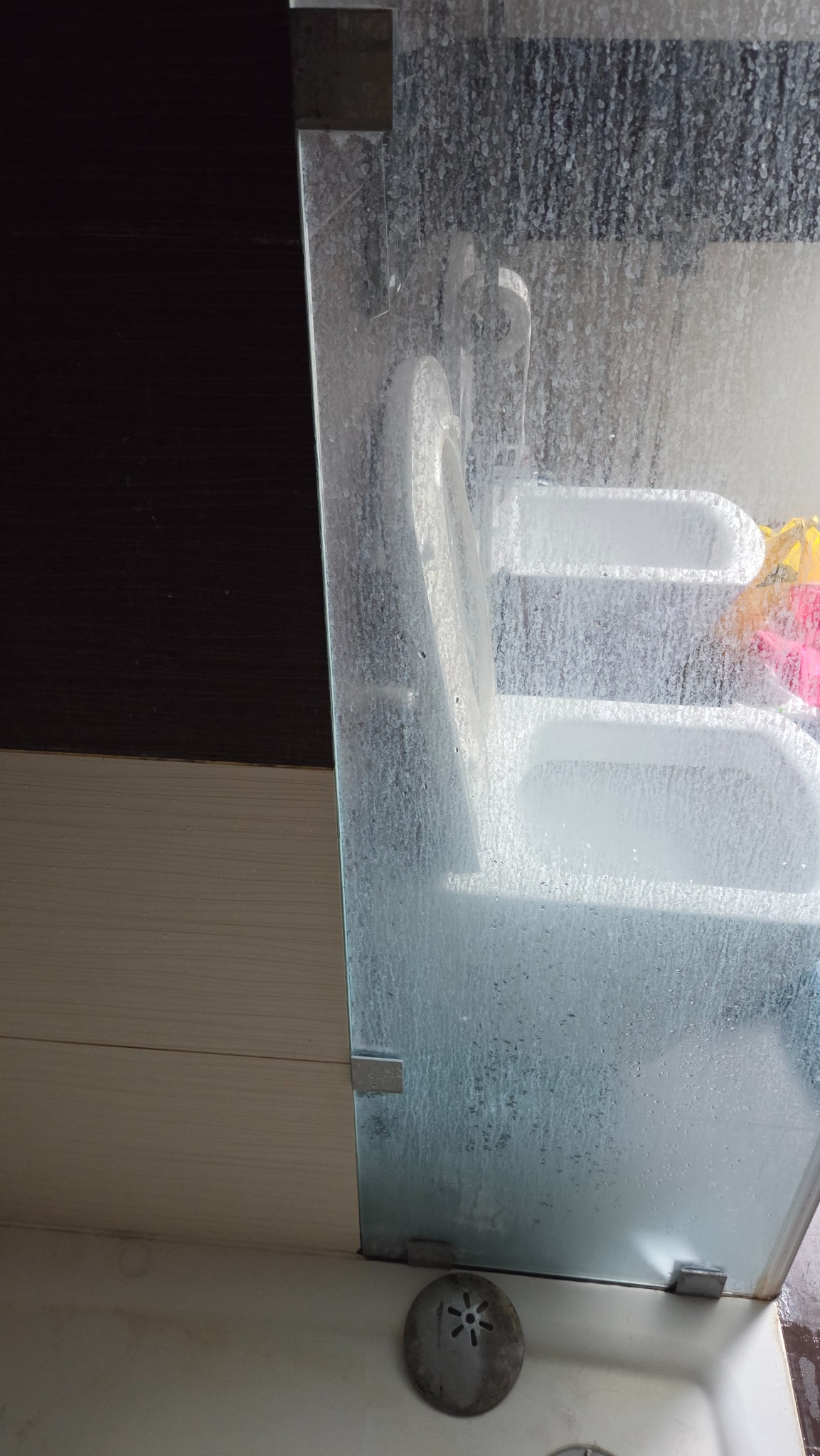 Zabrudzona kabina prysznicowa z widocznymi zaciekami i osadem, ukazująca potrzebę dokładnego czyszczenia. Widoczny odpływ i fragment umywalki.